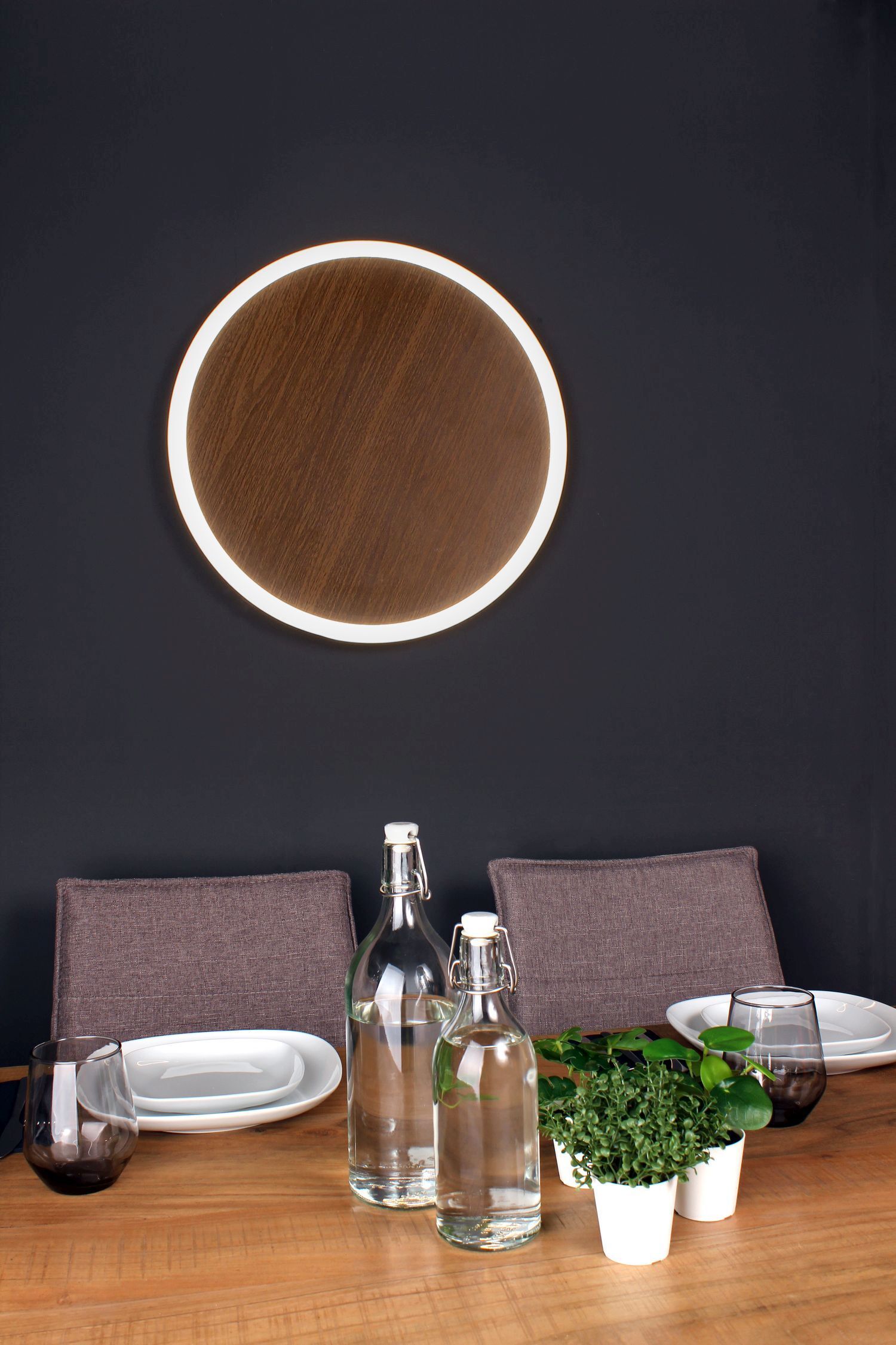 Wandleuchte, runder Spiegel, Holztisch, Glasflaschen, kleine Topfpflanze
